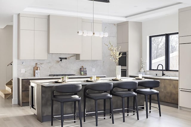 kitchen featuring a kitchen island, a sink, light countertops, hanging light fixtures, and modern cabinets