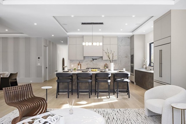 kitchen featuring a raised ceiling, a large island, modern cabinets, hanging light fixtures, and light countertops