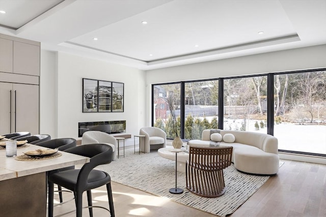 living area featuring a baseboard radiator, recessed lighting, a raised ceiling, light wood finished floors, and a glass covered fireplace