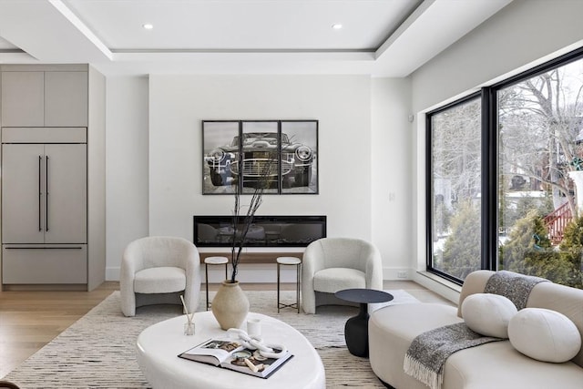 living area with light wood-type flooring, baseboards, a tray ceiling, and recessed lighting