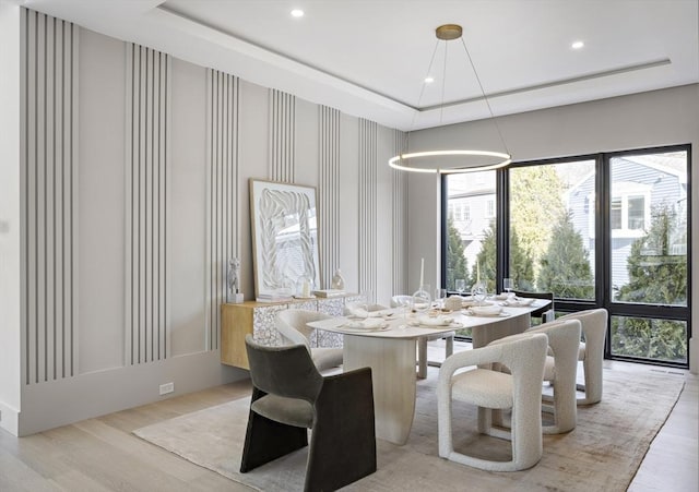 dining space with light wood-type flooring, a raised ceiling, and recessed lighting