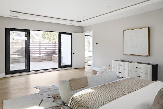 bedroom featuring access to outside, visible vents, light wood-style flooring, and a tray ceiling