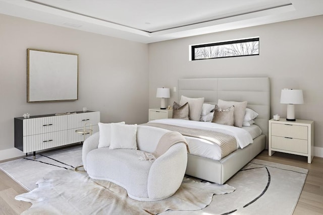 bedroom featuring a tray ceiling, light wood finished floors, and baseboards