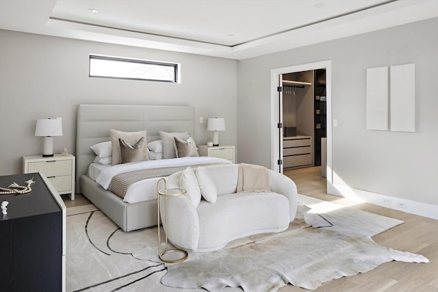 bedroom featuring a tray ceiling, a walk in closet, light wood finished floors, a closet, and baseboards