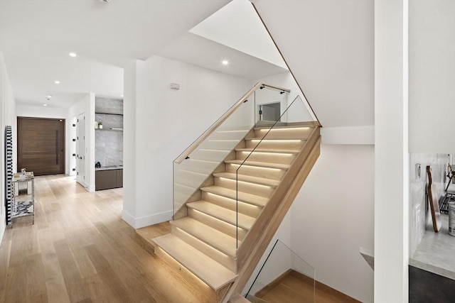 stairway with baseboards, wood finished floors, and recessed lighting