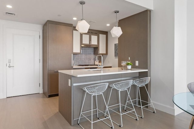 kitchen with sink, a kitchen breakfast bar, decorative backsplash, decorative light fixtures, and kitchen peninsula