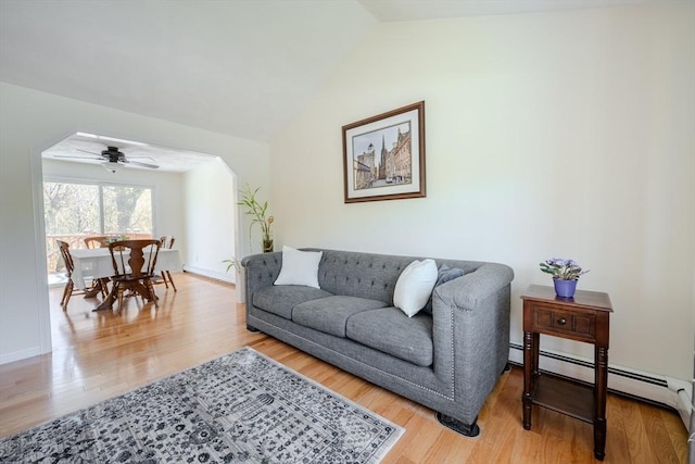 living area featuring lofted ceiling, baseboards, a baseboard heating unit, a ceiling fan, and light wood-style flooring