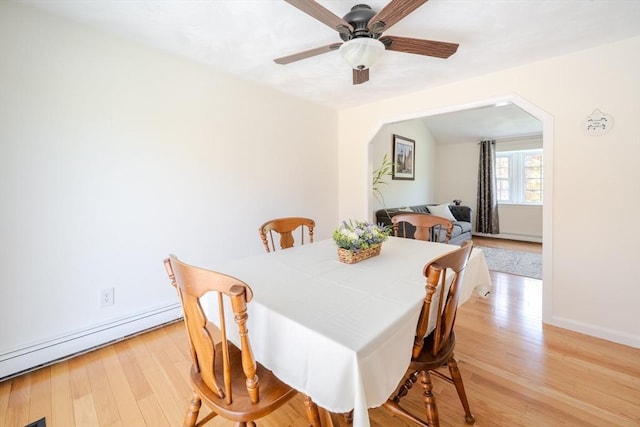 dining area with ceiling fan, arched walkways, light wood-type flooring, baseboards, and a baseboard heating unit