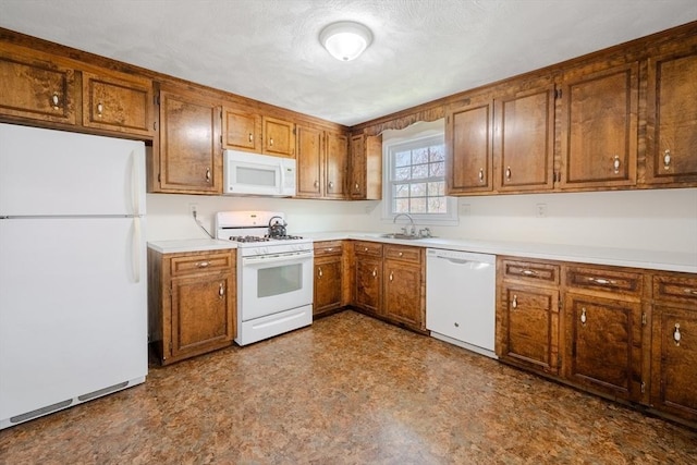 kitchen with a sink, light countertops, brown cabinetry, and white appliances