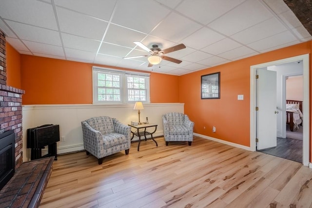 sitting room featuring a ceiling fan, wainscoting, wood finished floors, a baseboard radiator, and a drop ceiling