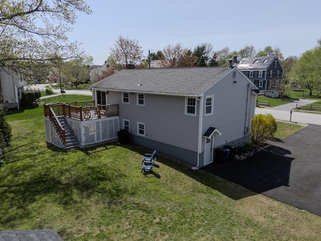 back of property with a lawn, a shingled roof, a wooden deck, and stairway