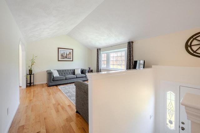 living area featuring light wood-style floors, baseboards, and lofted ceiling