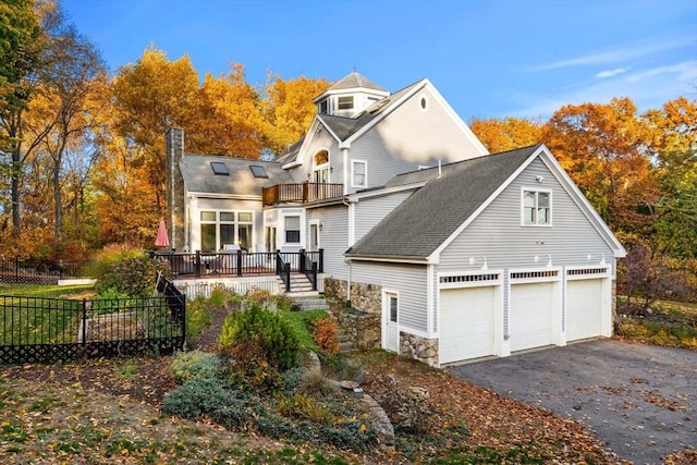 back of house featuring stone siding, a chimney, aphalt driveway, an attached garage, and fence