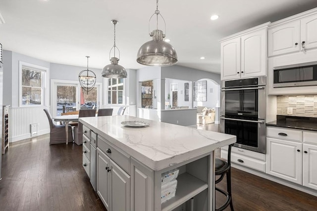 kitchen with arched walkways, a kitchen island, white cabinetry, appliances with stainless steel finishes, and dark wood finished floors