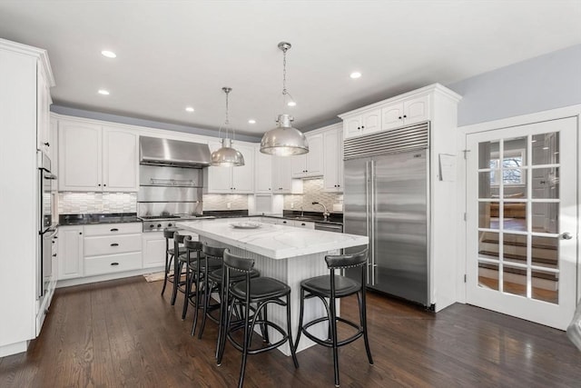kitchen featuring a breakfast bar area, stainless steel appliances, a sink, a center island, and wall chimney exhaust hood