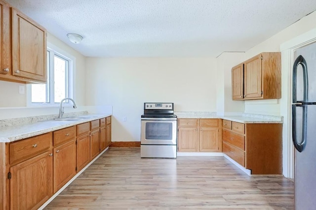kitchen featuring stainless steel appliances, a sink, light wood-style floors, a textured ceiling, and light countertops
