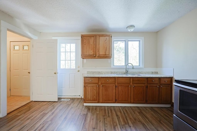 kitchen with a sink, stainless steel electric range, wood finished floors, a textured ceiling, and brown cabinets