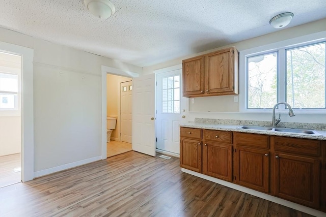 kitchen with a sink, a textured ceiling, wood finished floors, brown cabinets, and baseboards