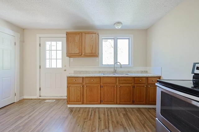 kitchen with electric stove, a sink, light wood finished floors, plenty of natural light, and a textured ceiling