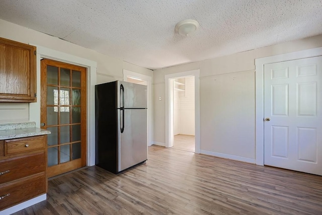 kitchen featuring freestanding refrigerator, brown cabinets, wood finished floors, and a textured ceiling