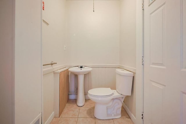bathroom featuring a wainscoted wall, toilet, tile patterned flooring, and a sink