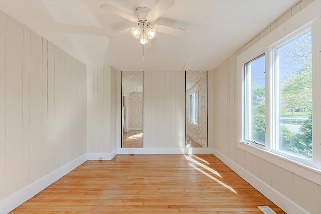 empty room featuring light wood-type flooring, ceiling fan, baseboards, and wooden walls