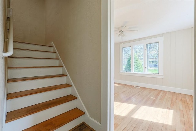 staircase featuring wood finished floors, a ceiling fan, and baseboards