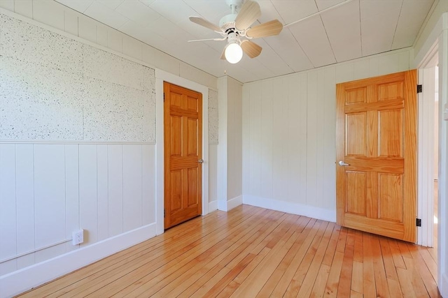spare room with light wood-type flooring, a ceiling fan, baseboards, and a wainscoted wall