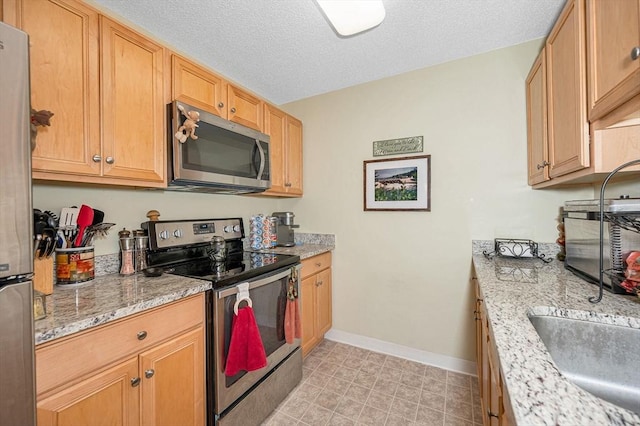 kitchen with a textured ceiling, light stone counters, stainless steel appliances, and baseboards
