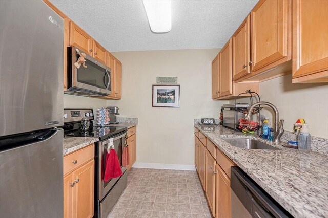 kitchen with light stone countertops, appliances with stainless steel finishes, a sink, baseboards, and a textured ceiling