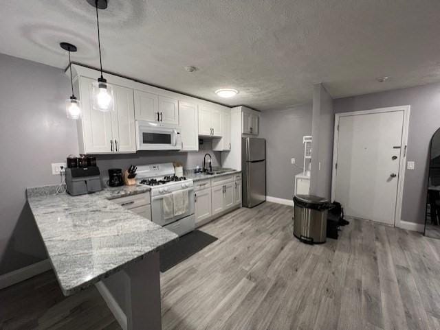 kitchen with light stone counters, decorative light fixtures, kitchen peninsula, white appliances, and white cabinets