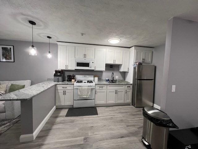 kitchen featuring sink, white appliances, white cabinets, decorative light fixtures, and kitchen peninsula