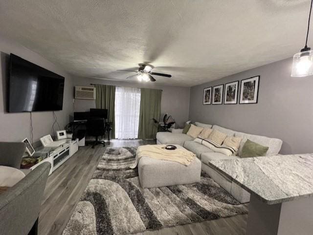 living room with dark hardwood / wood-style flooring, a wall mounted air conditioner, a textured ceiling, and ceiling fan