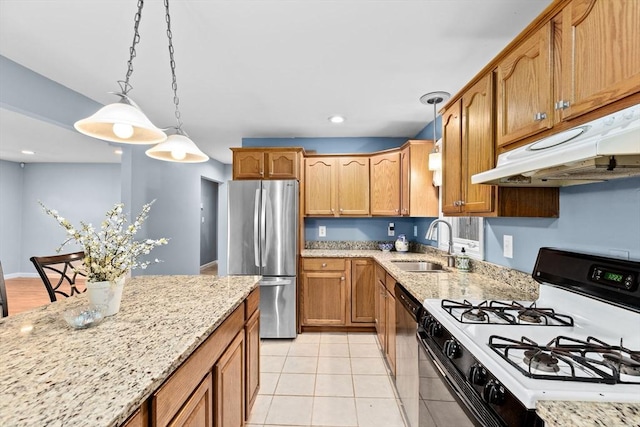 kitchen featuring gas stove, freestanding refrigerator, a sink, under cabinet range hood, and light stone countertops