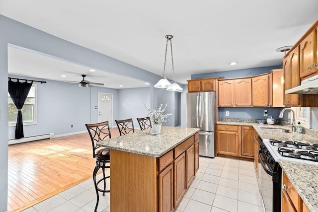 kitchen with a sink, freestanding refrigerator, a baseboard heating unit, a kitchen breakfast bar, and ceiling fan
