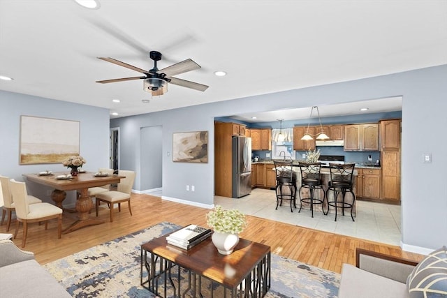 living room featuring recessed lighting, a ceiling fan, baseboards, and light wood-style flooring