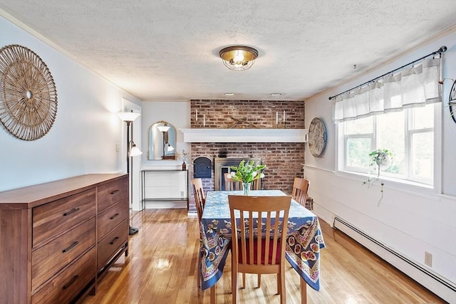 7 Squannacook Ter, Townsend, MA 01469 - dining room featuring a baseboard radiator, a textured ceiling, light wood-style flooring, brick wall, and a fireplace