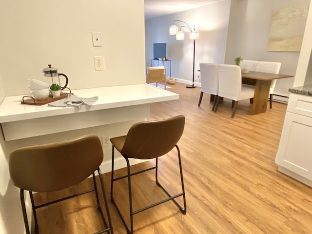 interior space with white cabinets, a kitchen breakfast bar, baseboard heating, and light hardwood / wood-style flooring