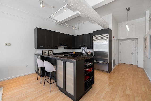 kitchen with open shelves, dark cabinetry, a towering ceiling, and built in fridge