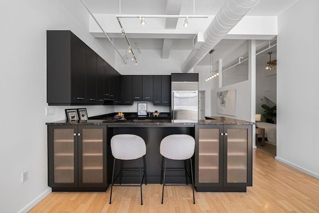 kitchen with light wood-style flooring, stainless steel built in refrigerator, a breakfast bar, and dark cabinetry