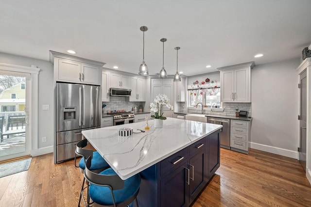 kitchen with a center island, light wood-type flooring, pendant lighting, stainless steel appliances, and light stone countertops