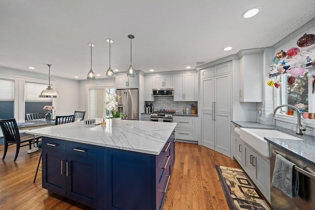 kitchen with a kitchen island, pendant lighting, sink, light stone counters, and stainless steel appliances