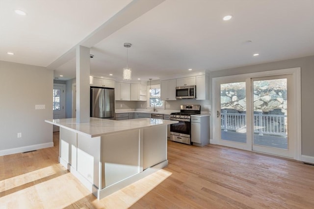 kitchen featuring pendant lighting, a center island, stainless steel appliances, light wood-type flooring, and white cabinetry