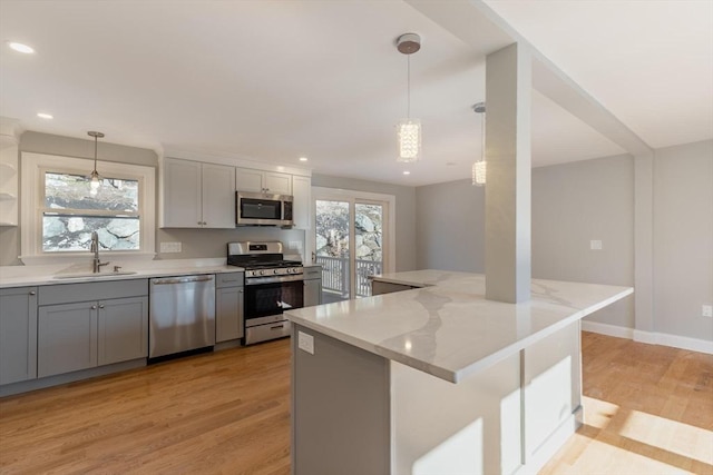 kitchen featuring sink, light stone counters, light wood-type flooring, pendant lighting, and appliances with stainless steel finishes