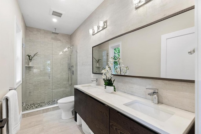 bathroom featuring a stall shower, toilet, double vanity, and tasteful backsplash