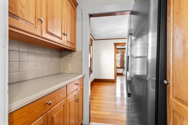 kitchen with backsplash, ornamental molding, stainless steel fridge, and light hardwood / wood-style floors