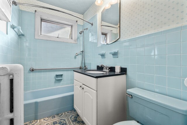 full bathroom with vanity, toilet, tiled shower / bath combo, and tile walls