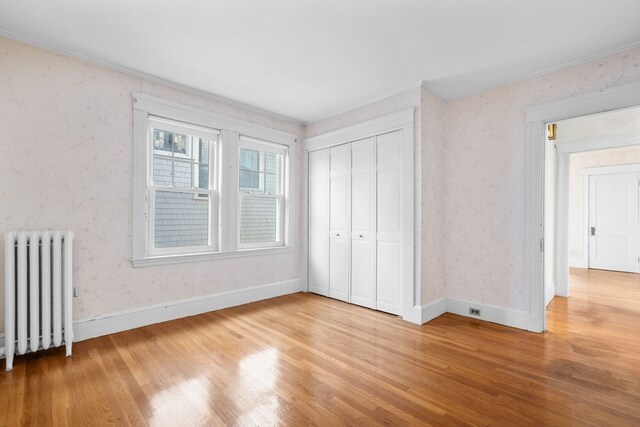 unfurnished bedroom featuring a closet, radiator heating unit, hardwood / wood-style flooring, and crown molding