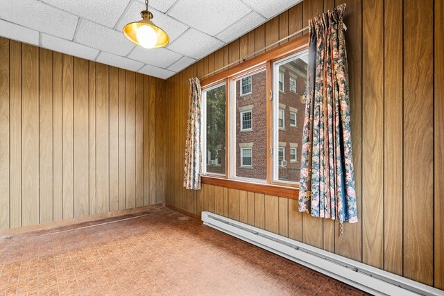 spare room with a baseboard radiator, wooden walls, and a paneled ceiling