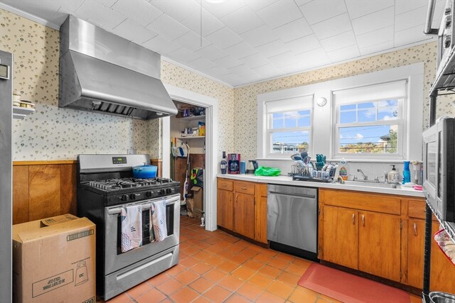 kitchen with wall chimney exhaust hood, stainless steel appliances, sink, crown molding, and light tile patterned floors